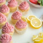 An array of strawberry lemonade cupcakes scattered next to fresh strawberries and cut lemon slices.