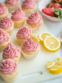 An array of strawberry lemonade cupcakes scattered next to fresh strawberries and cut lemon slices.