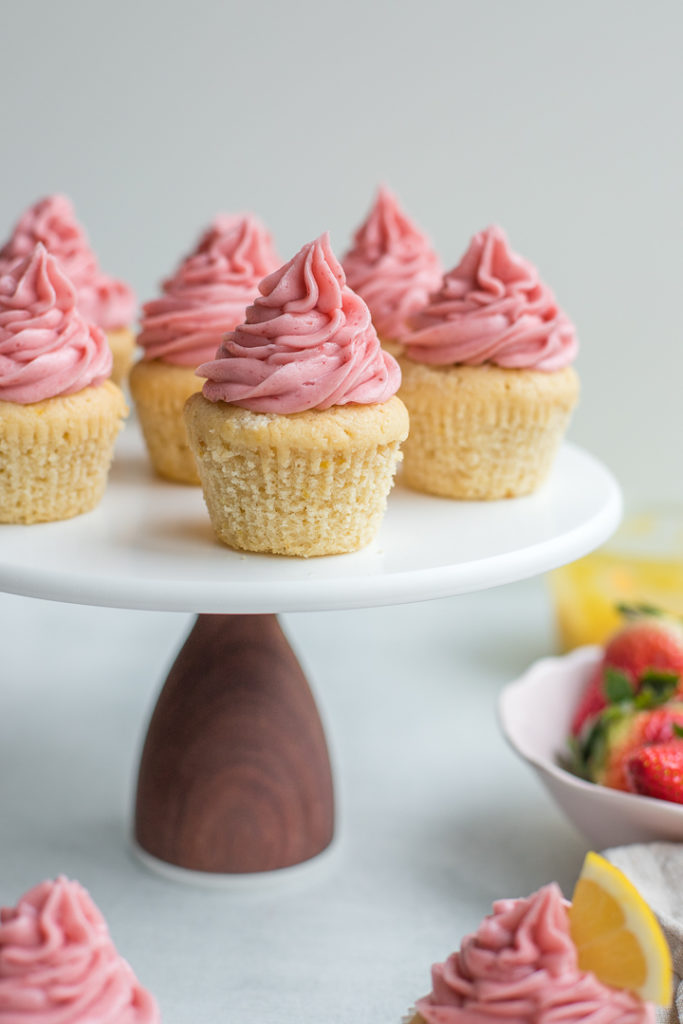 Strawberry lemonade cupcakes arranged on a white and walnut cake stand.