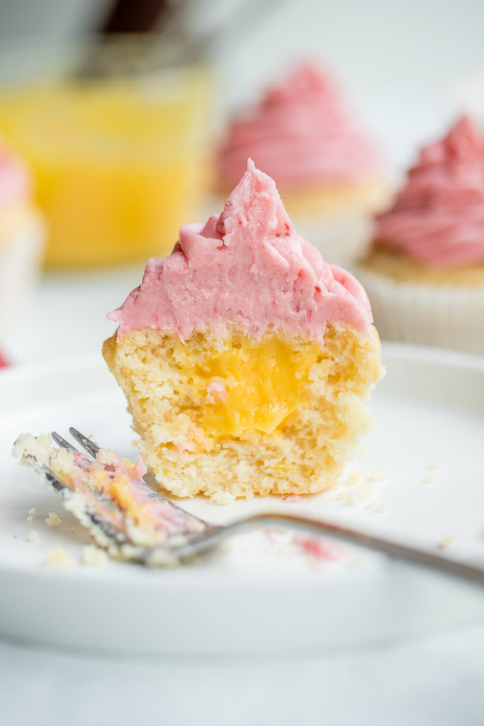 A filled lemon cupcake cut open to reveal a filling of creamy, bright lemon curd.