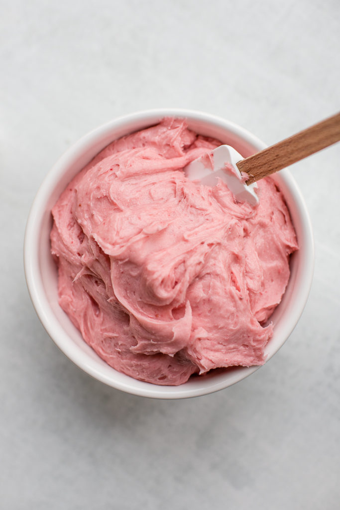 A white bowl filled with creamy, smooth, bright pink fresh strawberry frosting.