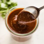 Spoon hovering a jar of thick homemade red enchilada sauce.