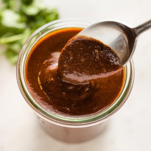 Spoon hovering a jar of thick homemade red enchilada sauce.