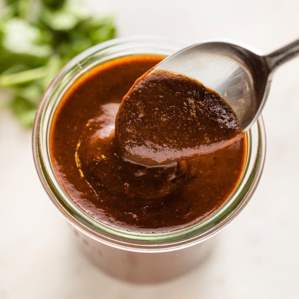 Spoon hovering a jar of thick homemade red enchilada sauce.