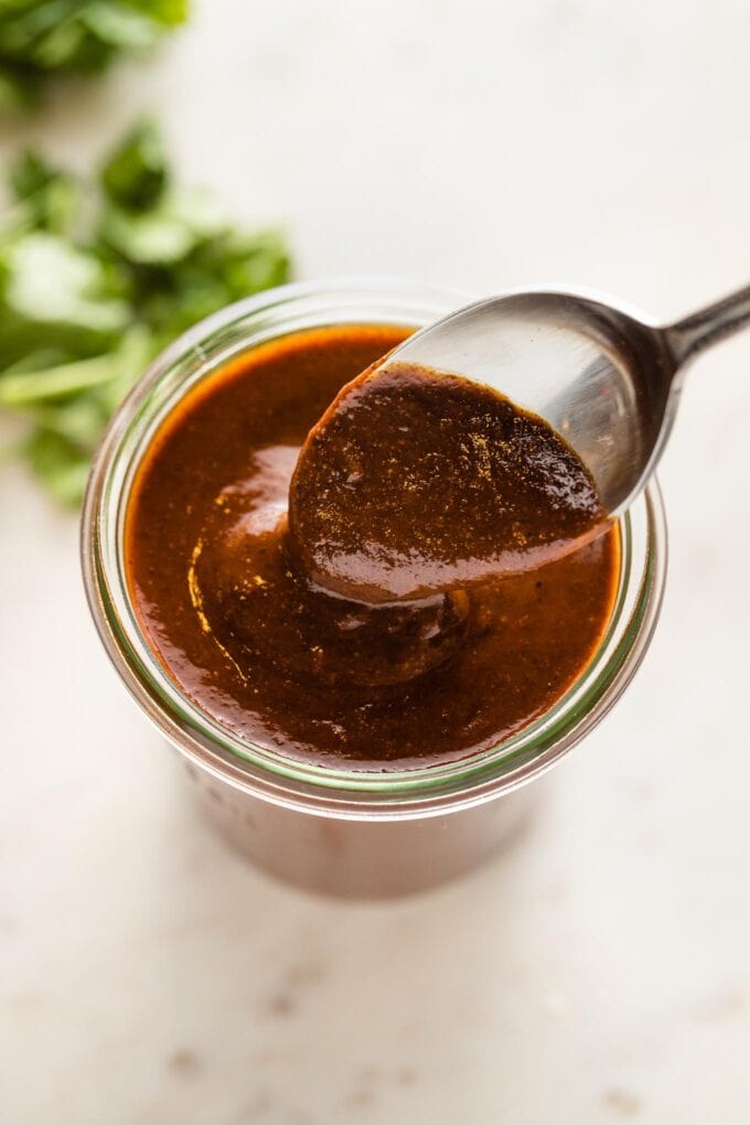 Spoon hovering a jar of thick homemade red enchilada sauce.