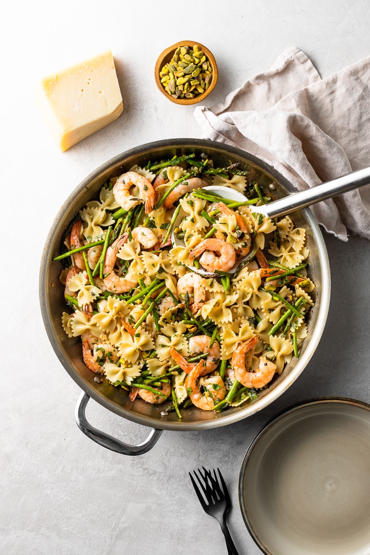 A large skillet filled with lemon asparagus pasta with shrimp and pistachios.