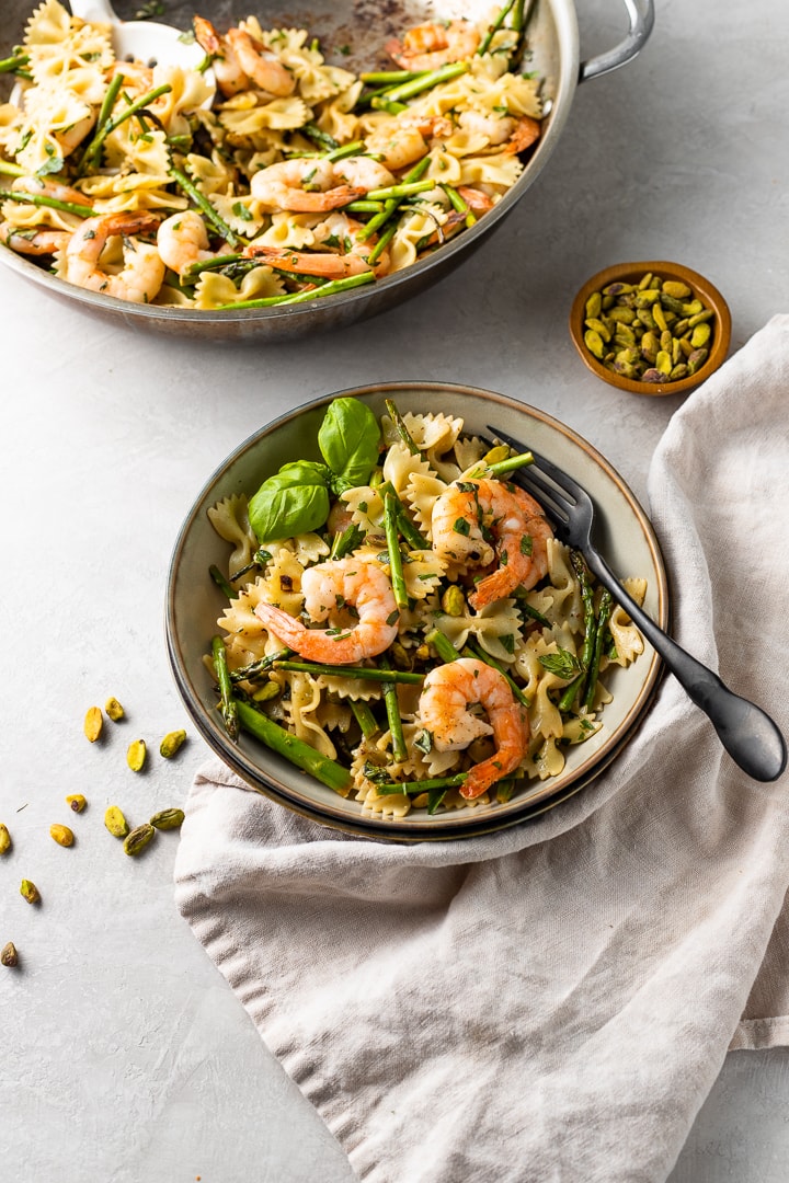 A small bowl filled with a generous serving of lemon asparagus pasta, topped with shrimp and garnished with fresh basil.