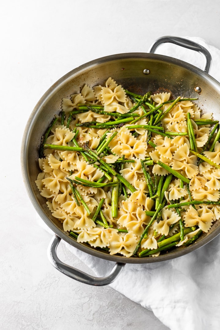 Cooking process photo showing cooked pasta and asparagus in a skillet.