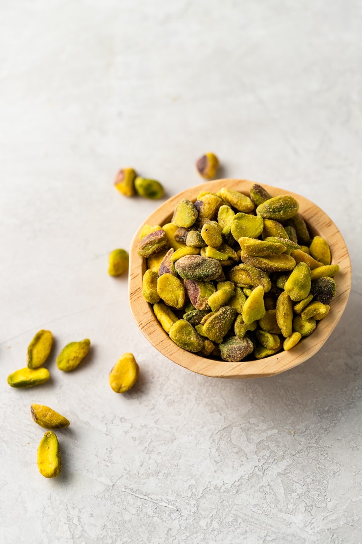 Close up image of shelled pistachios in a small wooden bowl.