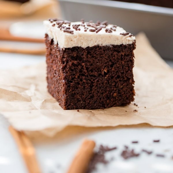 A small square slice of Mexican chocolate cake with cinnamon frosting and chocolate sprinkles, set on a piece of parchment paper.