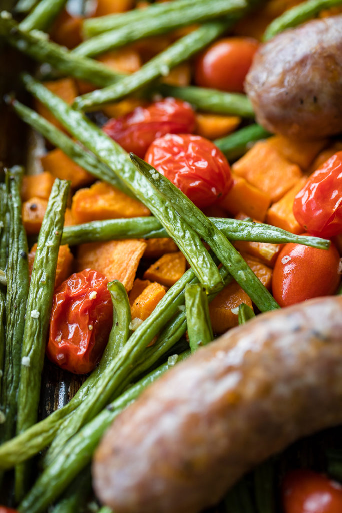 Close-up of crinkly roasted green beans, cherry tomatoes, and sweet potatoes.