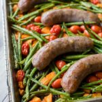 A pan filled with an Italian sausage sheet pan dinner with roasted sweet potatoes, green beans, and cherry tomatoes, fresh out of the oven and ready to serve.