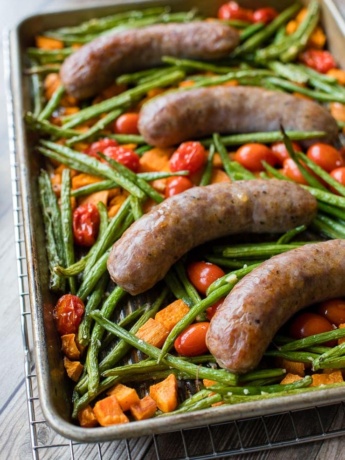 A pan filled with an Italian sausage sheet pan dinner with roasted sweet potatoes, green beans, and cherry tomatoes, fresh out of the oven and ready to serve.