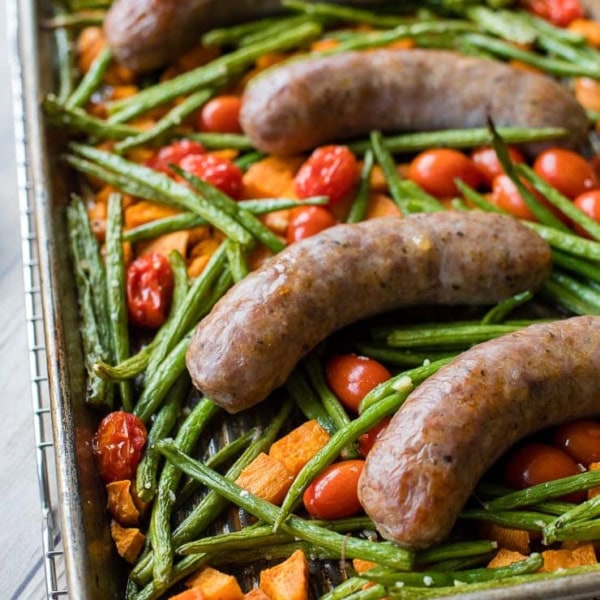 A pan filled with an Italian sausage sheet pan dinner with roasted sweet potatoes, green beans, and cherry tomatoes, fresh out of the oven and ready to serve.