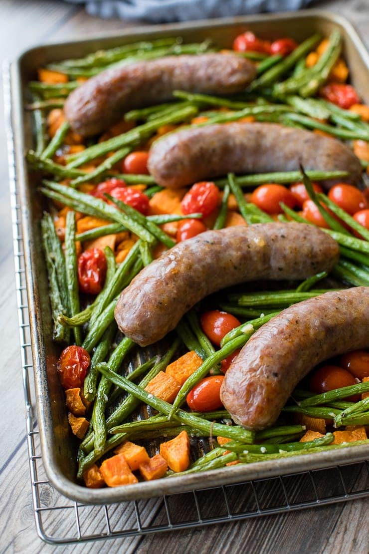 A pan filled with an Italian sausage sheet pan dinner with roasted sweet potatoes, green beans, and cherry tomatoes, fresh out of the oven and ready to serve.
