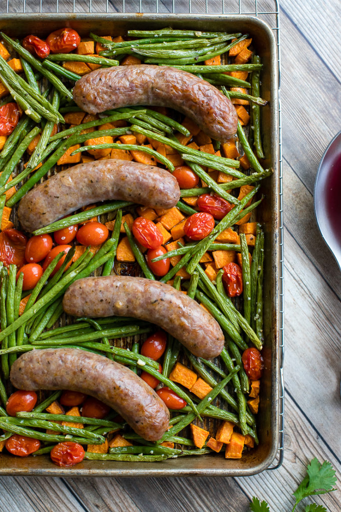 A pan filled with an Italian sausage sheet pan dinner with roasted sweet potatoes, green beans, and cherry tomatoes, fresh out of the oven and ready to serve.