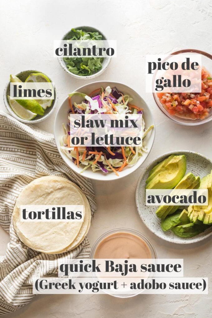 Labeled photo of prep bowls with slaw mix, limes, cilantro, pico de gallo, avocado, tortillas, and a simple Baja sauce.