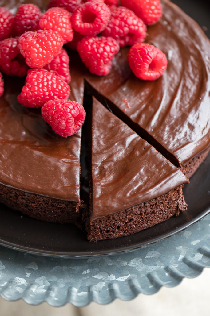 A just-cut slice of rich, perfect flourless chocolate cake with chocolate ganache and fresh raspberries.