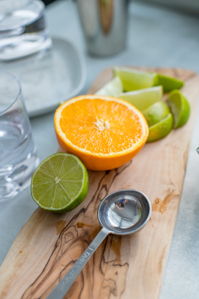 Cut oranges and limes on a cutting board, ready to be juiced for skinny margaritas.