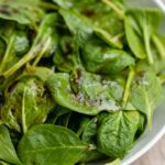 A large white bowl filled with balsamic spinach salad with sea salt.