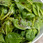 A large white bowl filled with balsamic spinach salad with sea salt.