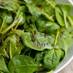 A large white bowl filled with balsamic spinach salad with sea salt.