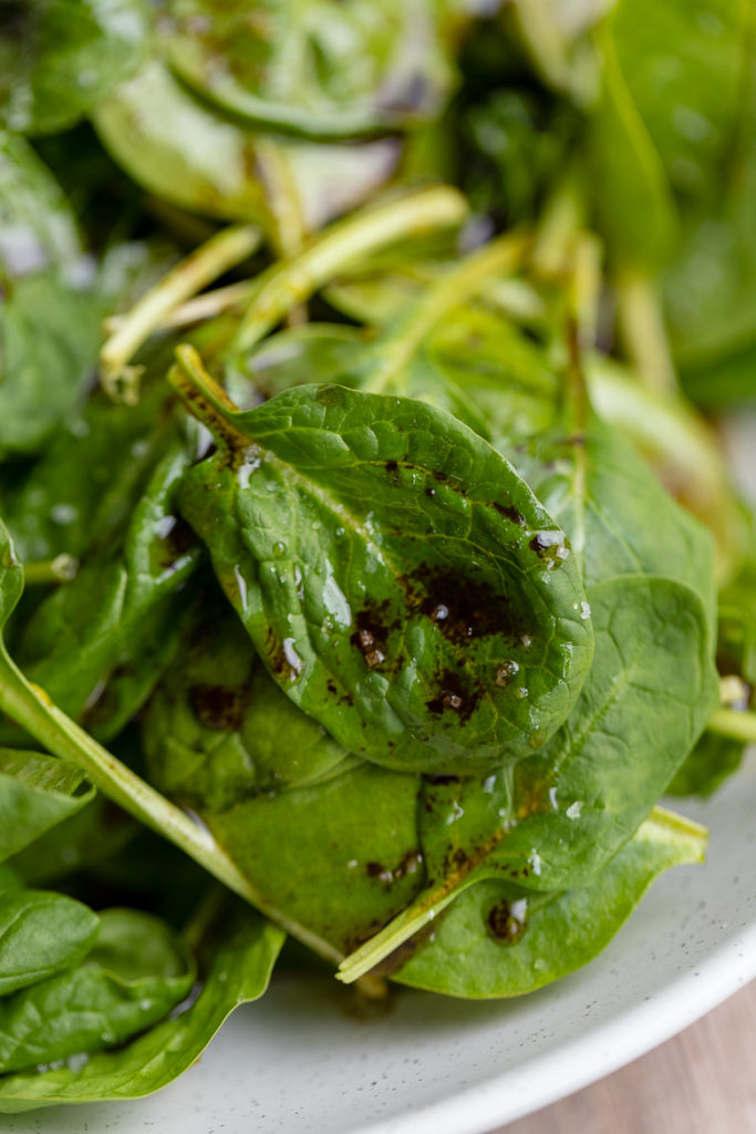 Close-up of balsamic spinach salad, a leaf of baby spinach drizzled in homemade balsamic vinaigrette.