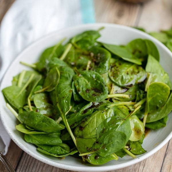 A bowl of balsamic spinach salad with sea salt, plated and ready for dinner.