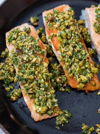 Three salmon filets topped with a pistachio herb mixture in the cast-iron pan in which they were seared.