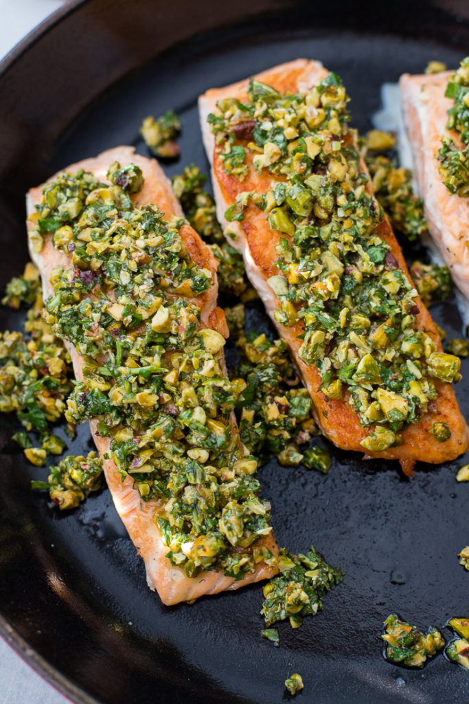 Three salmon filets topped with a pistachio herb mixture in the cast-iron pan in which they were seared.