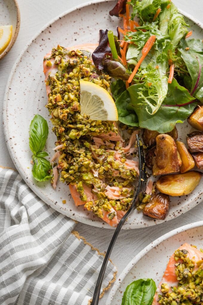 Close up of a flaky salmon fillet coated with a pistachio herb topping.