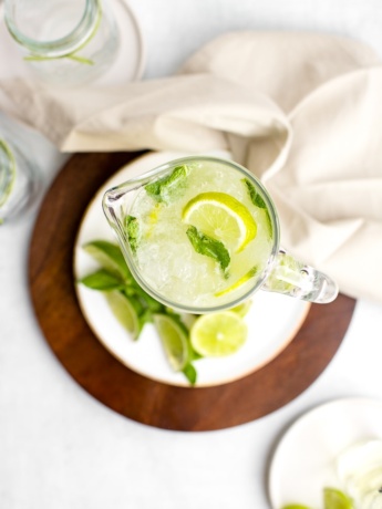 Overhead shot of a tall glass pitcher filled with sparkling limeade, garnished with lime wedges and mint.