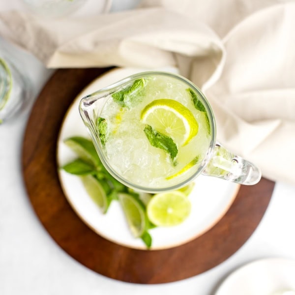 Overhead shot of a tall glass pitcher filled with sparkling limeade, garnished with lime wedges and mint.