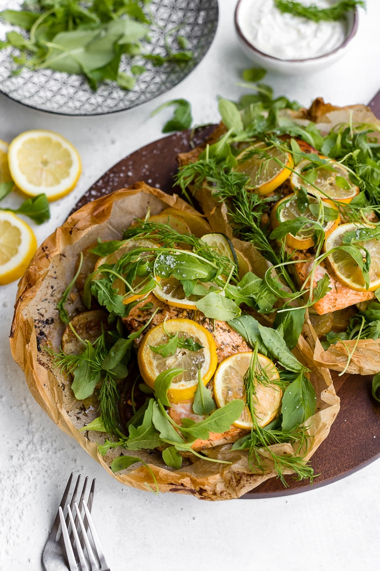 Parchment baked lemon salmon served in a packet with fresh arugula and herbs, served on a cutting board.