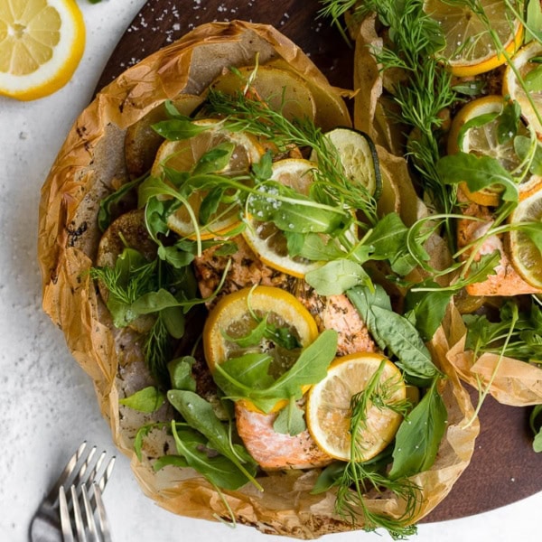 Parchment baked lemon salmon served in a packet with fresh arugula and herbs, served on a cutting board.