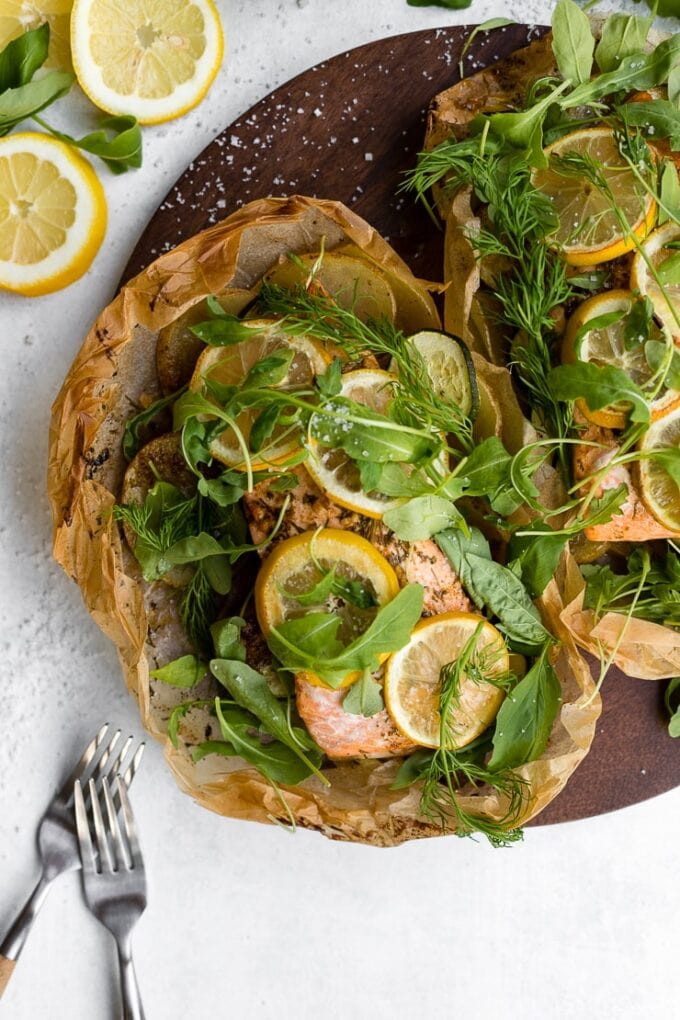 Parchment baked lemon salmon served in a packet with fresh arugula and herbs, served on a cutting board.