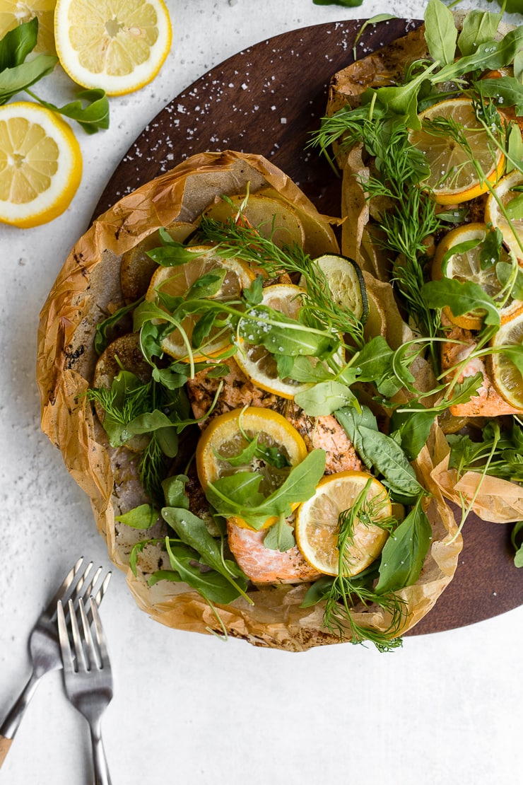 Two servings of parchment lemon salmon sprinkled with fresh dill, basil, and arugula.