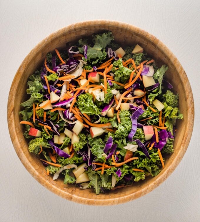 Cabbage, greens, carrot, and apple tossed together in a large wooden bowl.