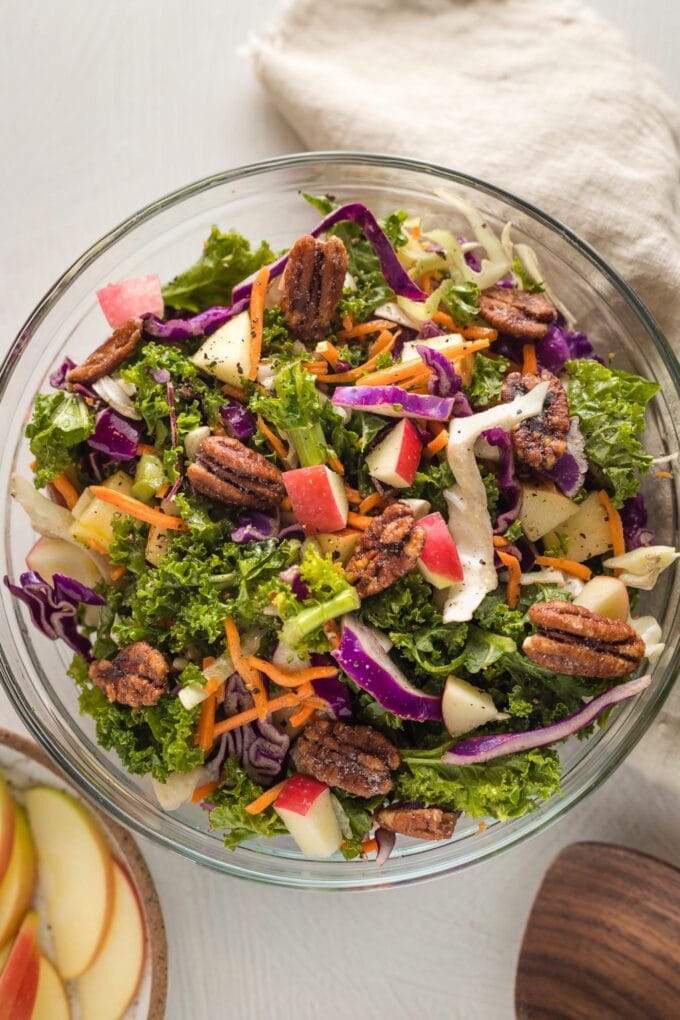 Apple cabbage slaw with shredded carrots and a brown sugar cider vinaigrette, served in a clear glass bowl.