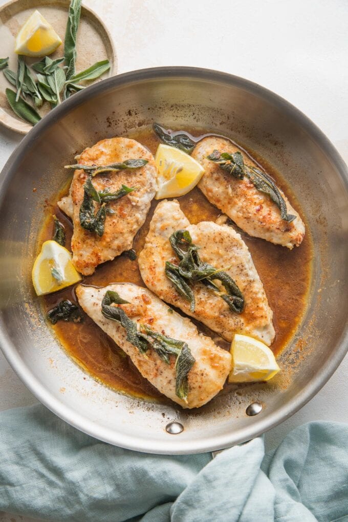 Overhead view of a skillet containing chicken breasts with a brown butter sage white wine sauce.