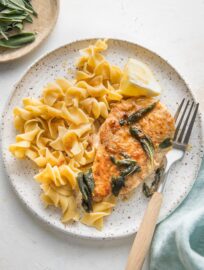 Small white plate with a serving of egg noodles and brown butter sage skillet chicken.