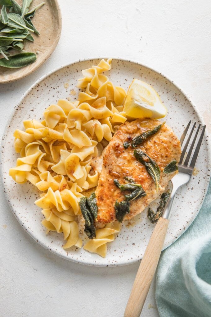 Small white plate with a serving of egg noodles and brown butter sage skillet chicken.