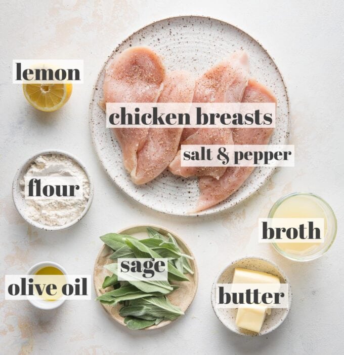 Labeled overhead photo of chicken breasts seasoned with kosher salt and black pepper, chicken broth, butter, fresh sage leaves, olive oil, flour, and half of a lemon, all in prep bowls and ready to cook.