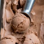 Close up of a metal ice cream scoop serving double chocolate ice cream.