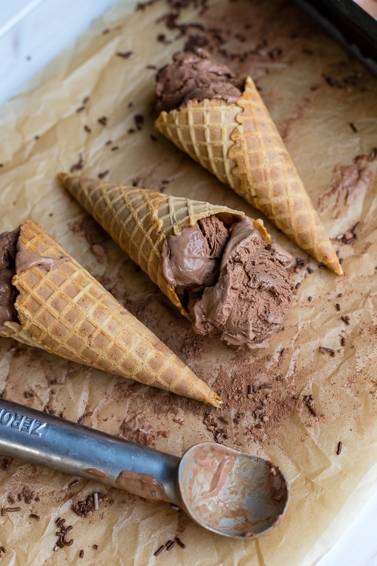 Three waffle cones filled with French style double chocolate ice cream, lying on parchment paper.