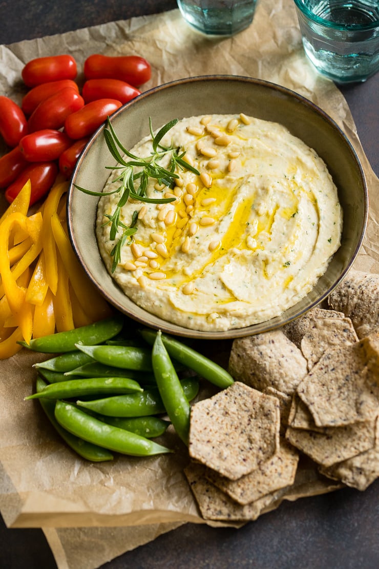 A bowl of garlic rosemary white bean dip surrounded by fresh veggies and chips.