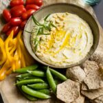 A bowl of garlic rosemary white bean dip surrounded by fresh veggies and chips.