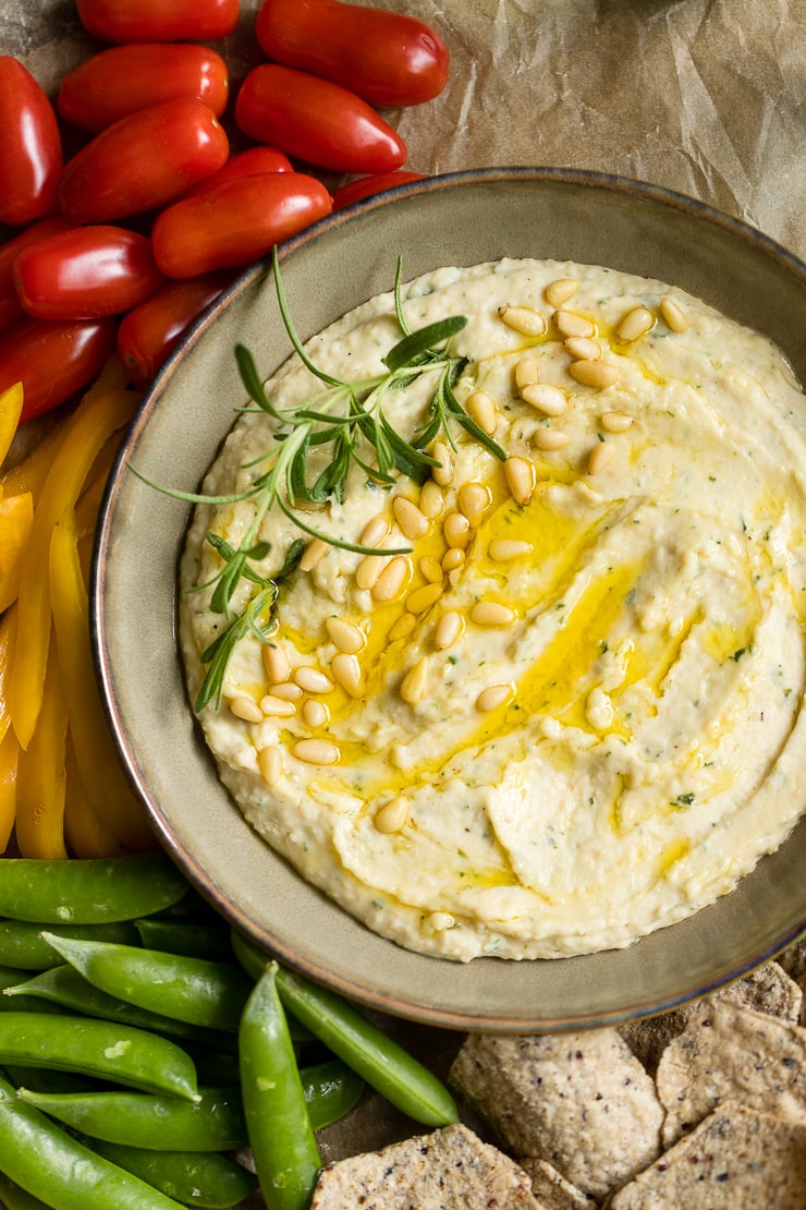 A bowl of garlic rosemary white bean dip surrounded by fresh veggies and chips.