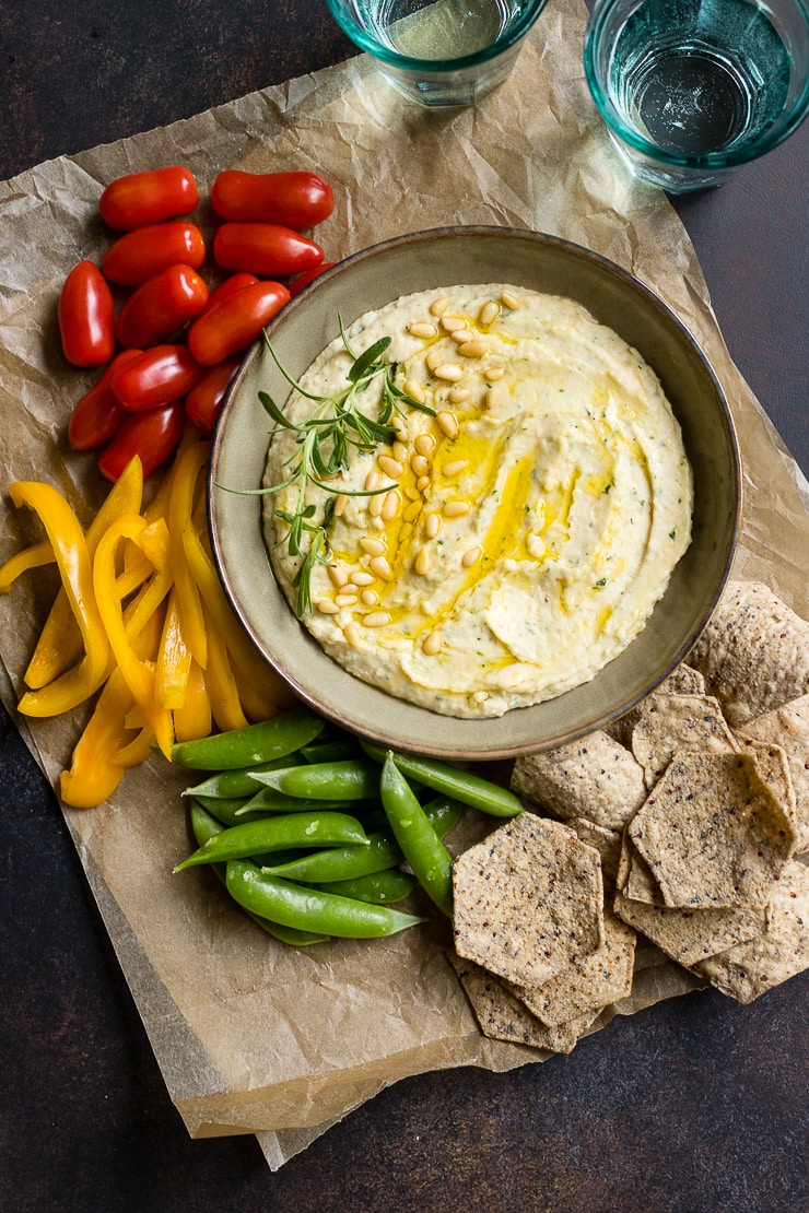 A bowl of garlic rosemary white bean dip surrounded by fresh veggies and chips.