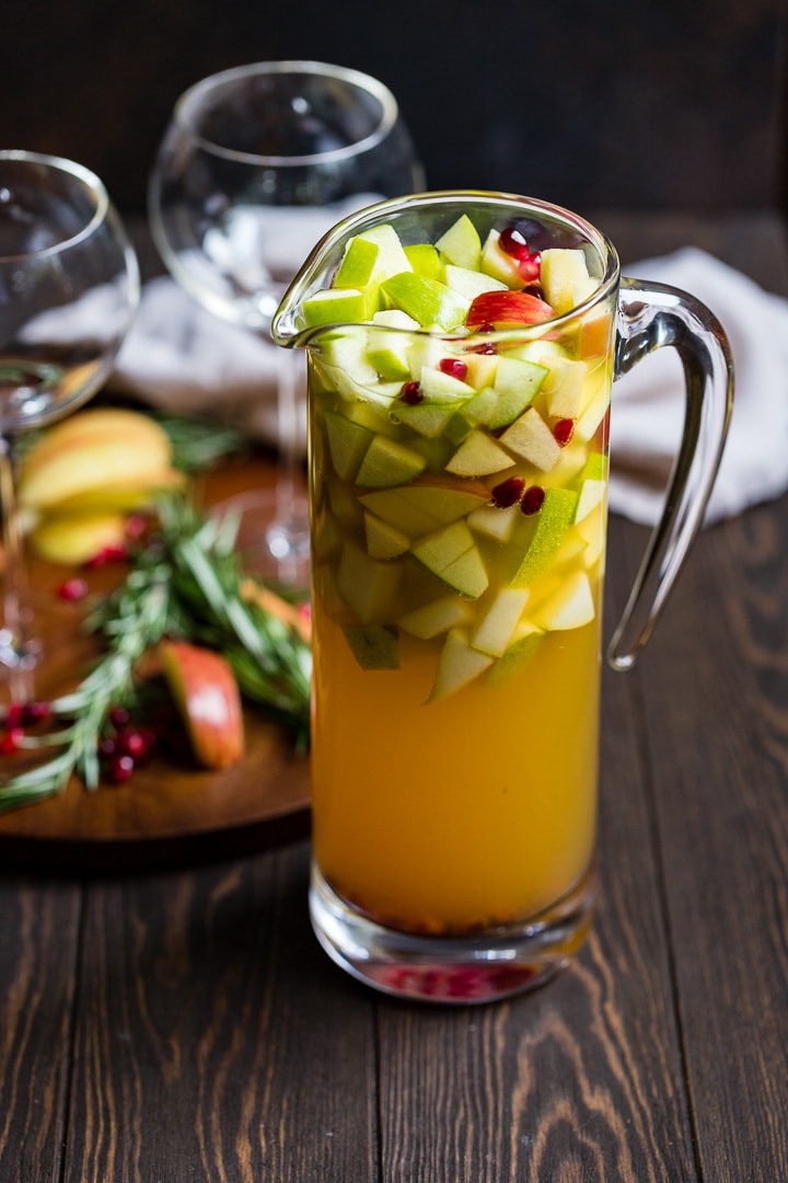 Large pitcher of autumn harvest white sangria with apples, pears, white wine, apple cider, and pomegranate seeds.